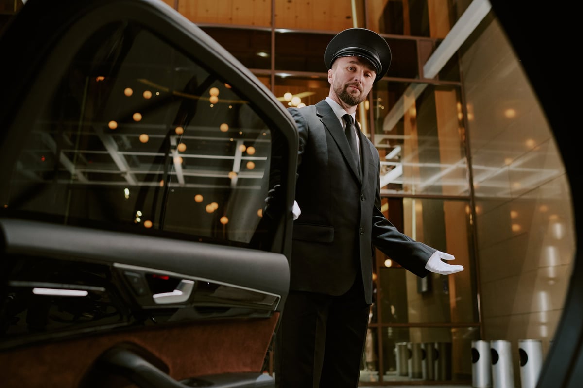 Professional chauffeur in uniform opening car door